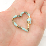Load image into Gallery viewer, A sterling silver heart-shaped carabiner clasp with black rhodium and gold plating, held in a person's hand.