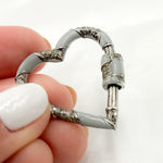 Load image into Gallery viewer, A sterling silver heart-shaped enamel carabiner clasp with black rhodium detailing held between fingers.