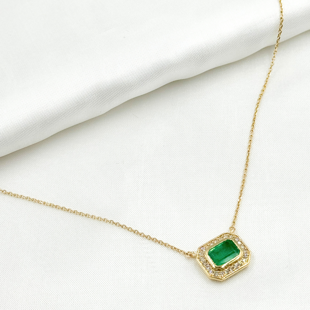 A 14k solid gold rectangle necklace with a green emerald and diamonds, displayed against a white background.