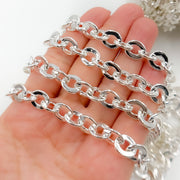 A person's hand holding a sterling silver hollow flat oval link chain.