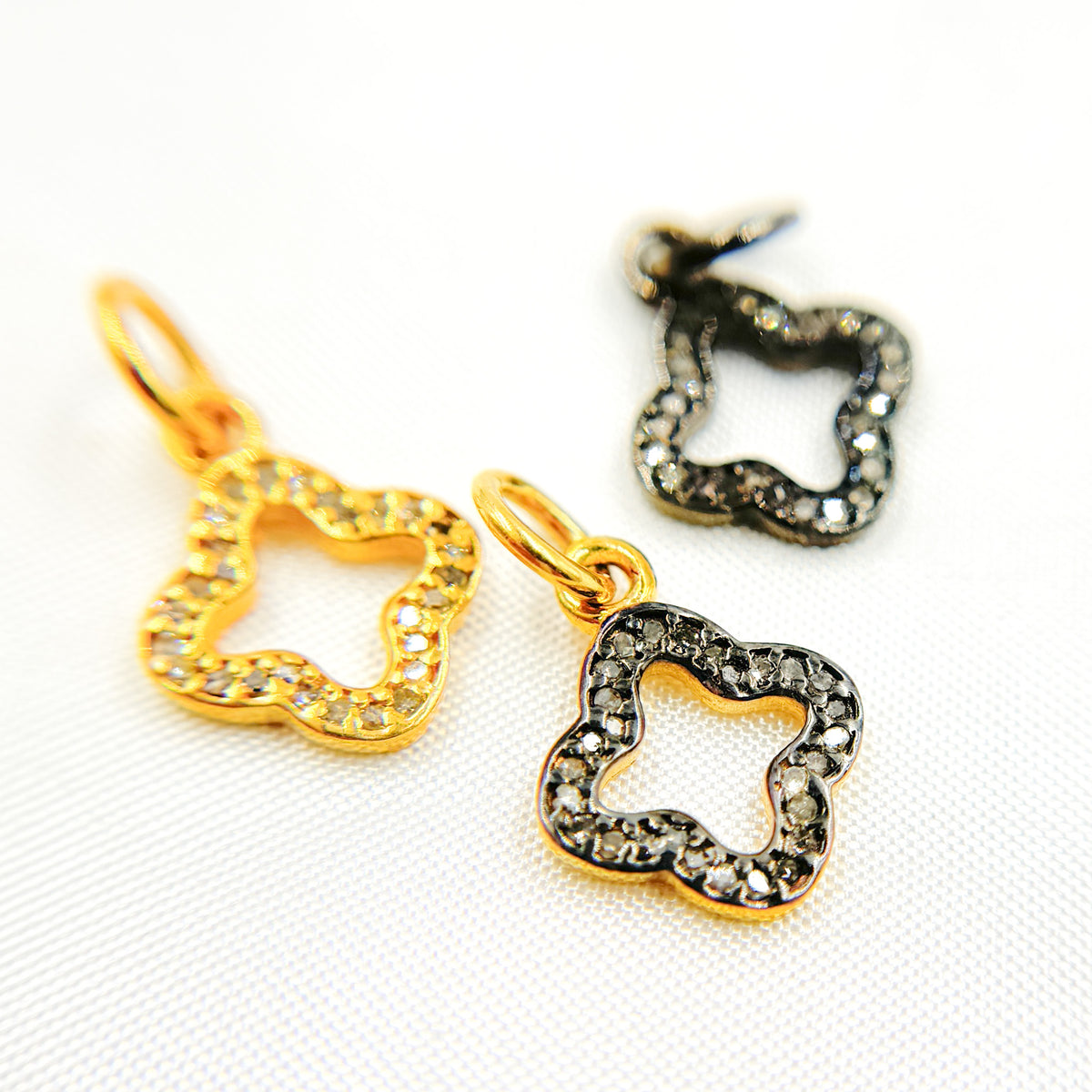 A set of three diamond sterling silver flower charms, one with black rhodium plating, one gold plated, and one rose gold plated, displayed against a white background.